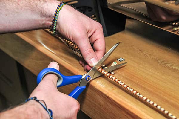 a person cutting LED strip light with a blue scissor